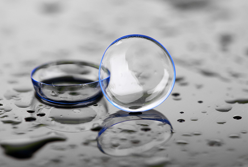 The image displays two clear, round objects with a reflective surface placed on a water droplet-covered surface, capturing the essence of dew or raindrops.