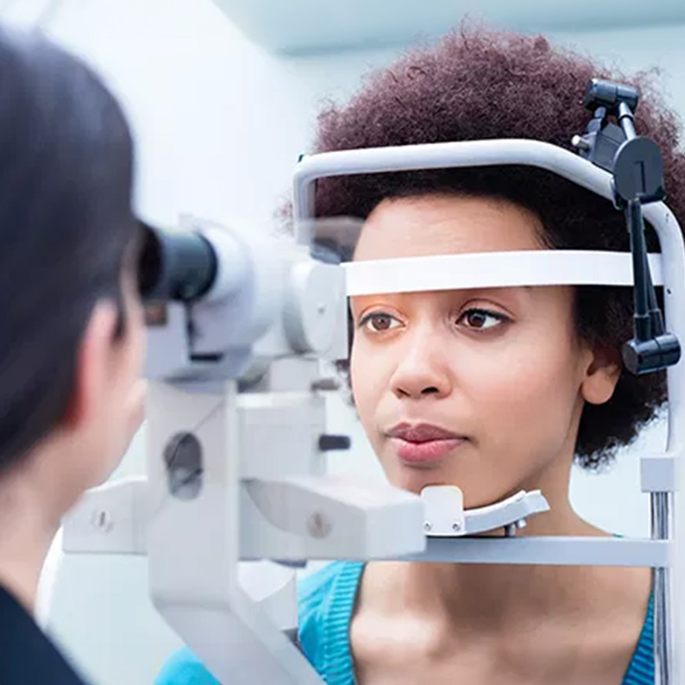 An adult woman receiving an eye exam with a medical professional using a slit lamp.